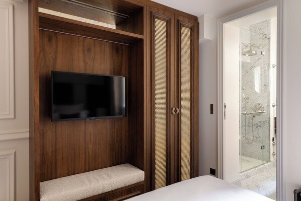 A bedroom with a TV mounted on a wooden wall, a bench, and a sliding door leading to a bathroom with a glass shower.