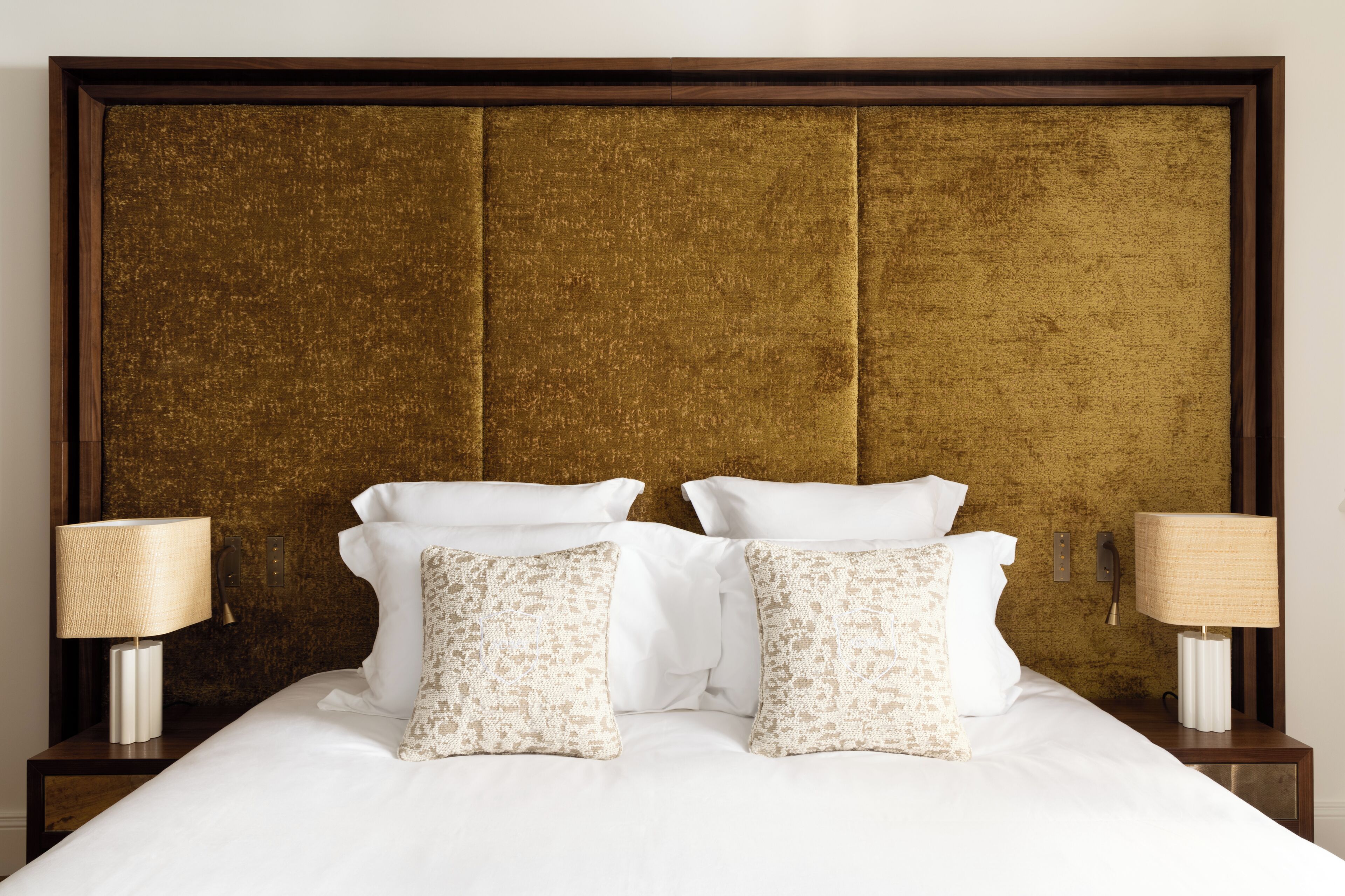 A bed with white linens, two decorative pillows, and two bedside lamps on either side.