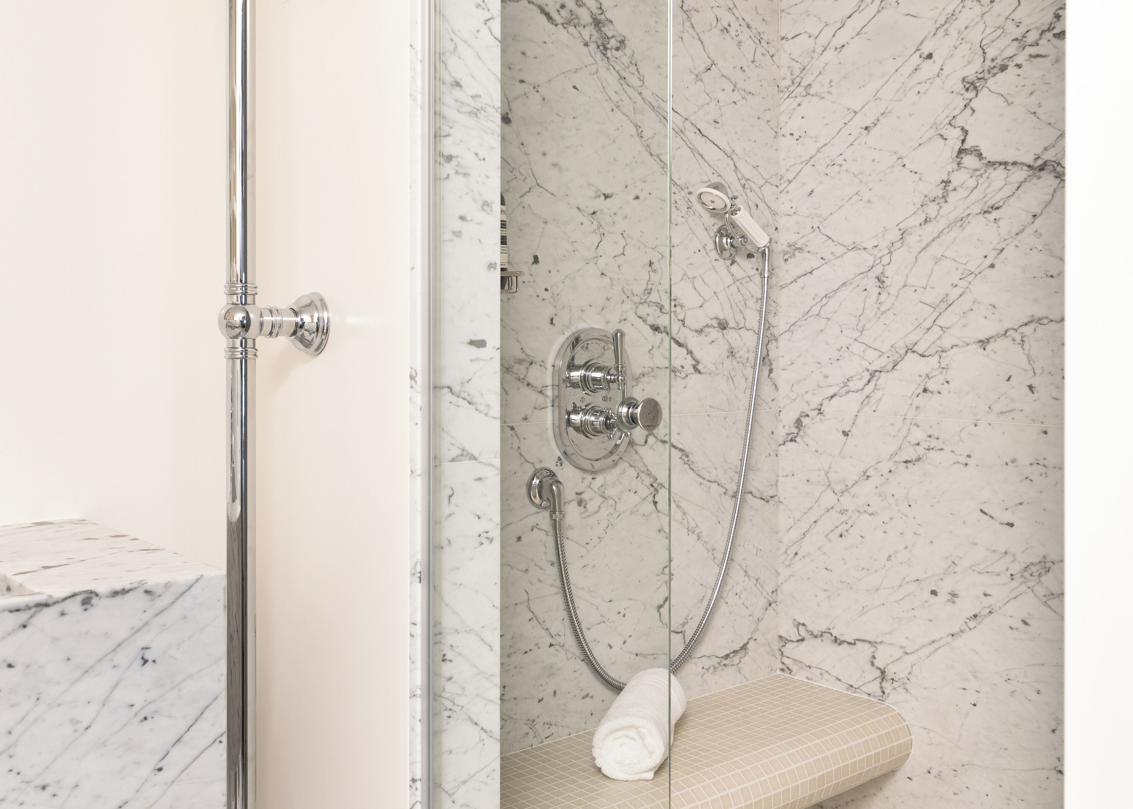 Ein Badezimmer mit Dusche, einer Marmorwand und einer Glastür.