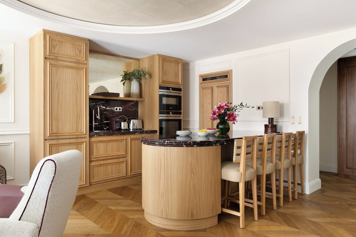 A kitchen with wooden cabinets, a marble countertop, and a central island with chairs.