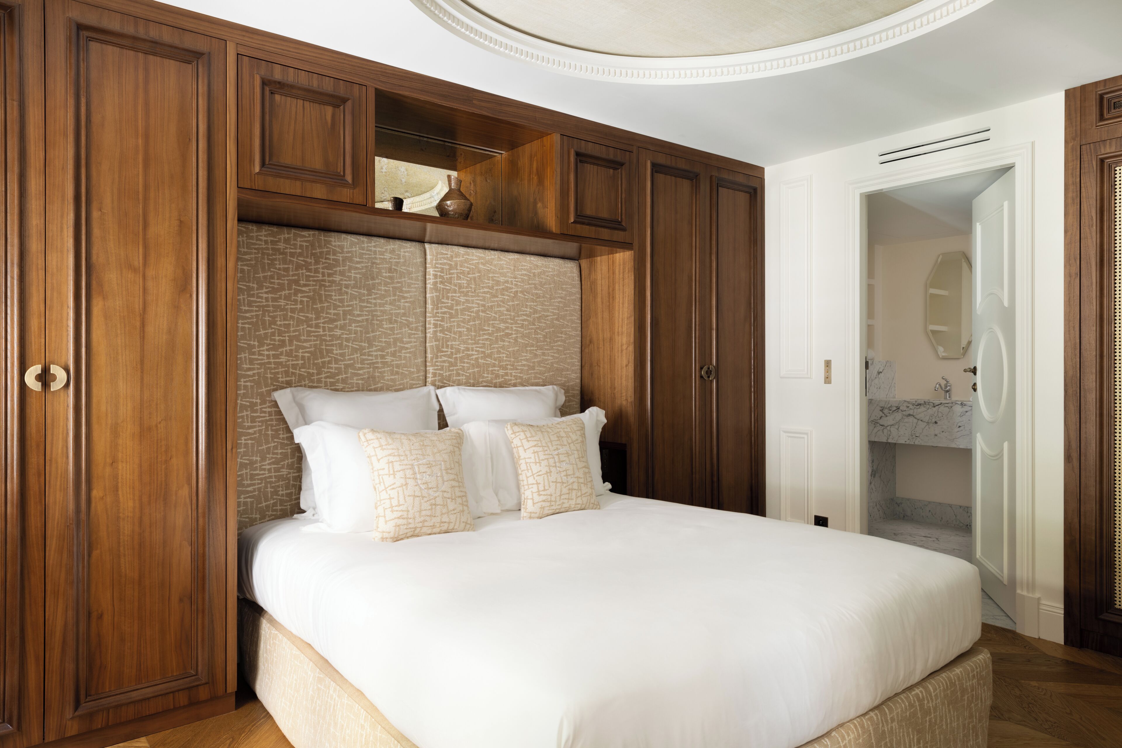 A bedroom with a large bed, wooden wardrobe, and a bathroom with a marble sink.