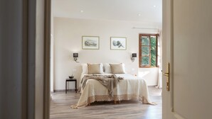 Quarto com cama, duas luzes fixadas na parede, uma mesinha com uma tigela e uma janela com cortinas.