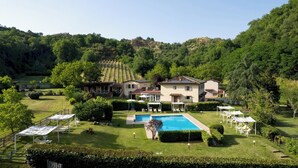 Uma casa grande com piscina, rodeada por vegetação exuberante e colinas.