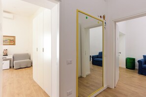 Una habitación con un espejo grande, un sillón gris, un sofá azul y una mesita de noche con una lámpara.