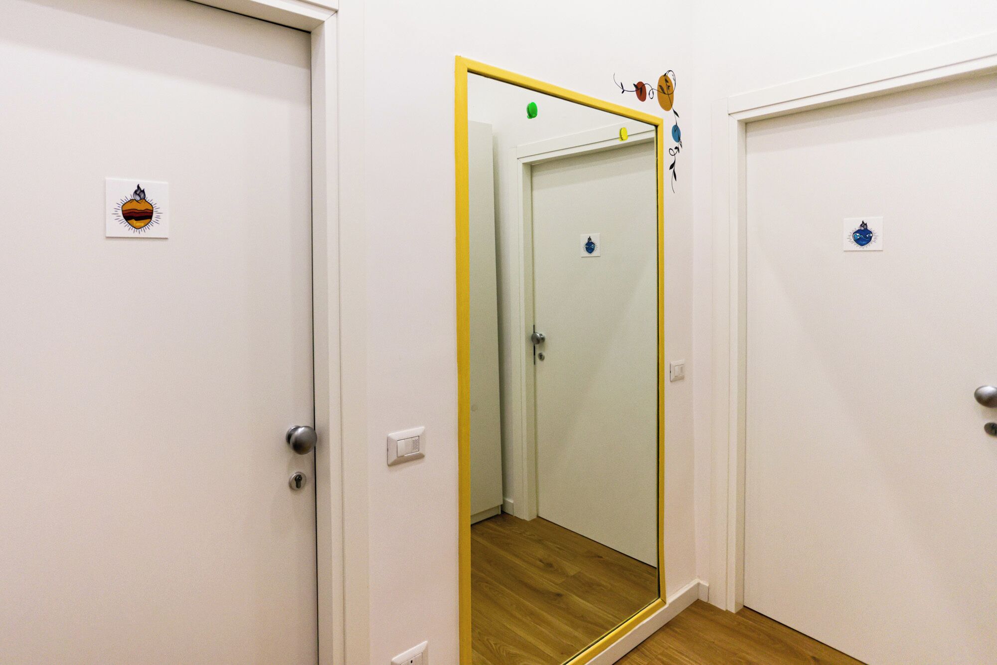 Passadís amb portes blanques, una de les quals té un mirall que reflecteix una porta amb un interruptor de llum i un petit senyal.