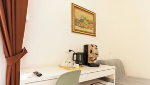 Ein Hotelzimmer mit weißem Schreibtisch, einer Kaffeemaschine, einer Fernbedienung und einem Bett mit gesteppter Bettdecke.