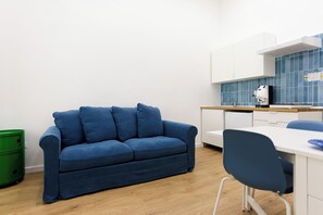 Une petite cuisine équipée avec un plan de travail blanc, une chaise bleue et un canapé bleu.