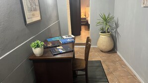 Un pasillo con un escritorio, una silla, plantas en macetas y cuadros en las paredes.