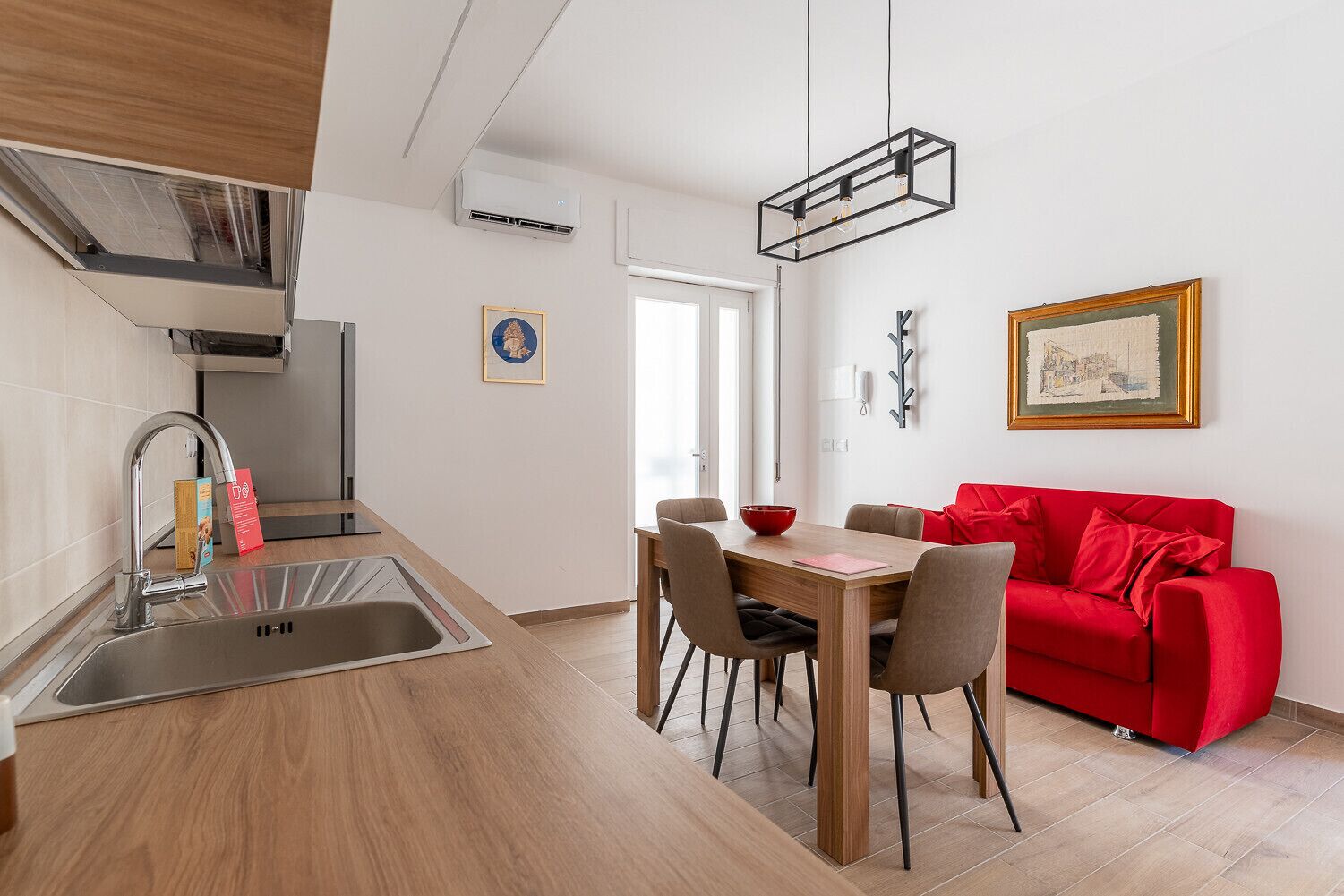 Eine moderne Küche mit Spüle, einem Esstisch mit Stühlen und einem roten Sofa.