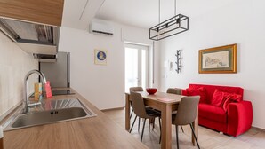 A modern kitchen with a sink, a dining table with chairs, and a red sofa. - Russu Suli Apartment 2 by Wonderful Italy (Siracusa)