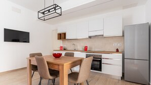 A modern kitchen with a wooden dining table, chairs, a red bowl, a stainless steel refrigerator, and a built-in oven. - Russu Suli Apartment 2 by Wonderful Italy (Siracusa)