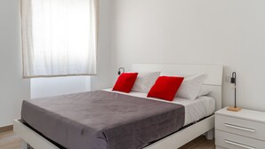 A modern bedroom with a bed, white nightstands, a bedside table, and a window with sheer curtains. - Russu Suli Apartment 2 by Wonderful Italy (Siracusa)