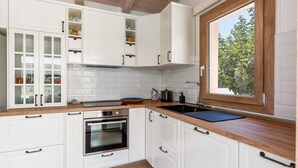Una cocina moderna con armarios blancos, encimera de madera, horno integrado, un lavabo y una ventana con vistas a árboles.