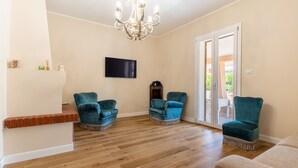 Amplia sala de estar con pisos de madera, un candelabro y dos sillones color turquesa.