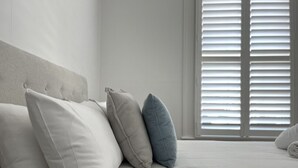 A neatly made bed with pillows, a headboard, and a window with blinds.