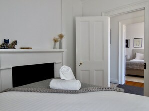 A bedroom with a bed, a white door, a fireplace, and a hallway leading to another room.