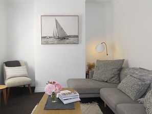 Un salon avec un canapé gris, un fauteuil, une table basse avec des livres et des fleurs, un tableau encadré au mur et une lampe.