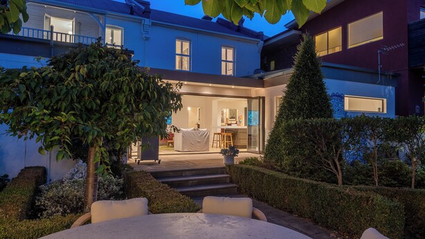 Una casa de dos pisos con un patio, un comedor y una cocina visibles a través de las ventanas.