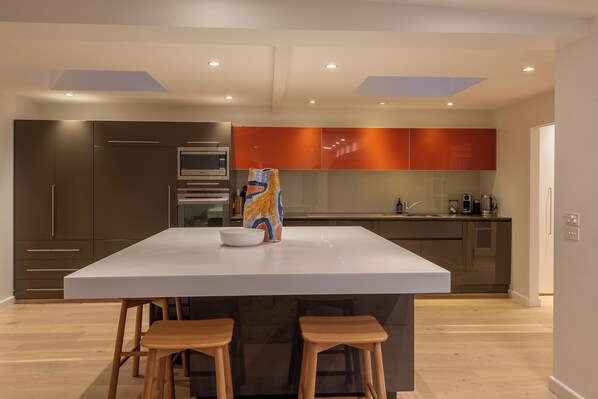 Cocina moderna con una isla grande, taburetes de madera y un microondas.