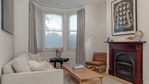 Una sala de estar con un sofá, una mesa de centro de madera, una chimenea y un ventanal con cortinas.