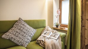 Vihreä sohva, jossa on kuviollinen koristetyyny, peitto ja valokuvia sisältävä kirja.