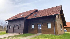 Een houten gebouw met twee verdiepingen, voorzien van een rode pannendak, een voordeur en een klein raam.