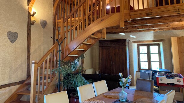 Un escalier en bois menant à une mezzanine, une table à manger avec des chaises et une table de baby-foot.