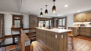 Cocina amplia con armarios de madera, una isla central, luces colgantes y vistas al exterior.