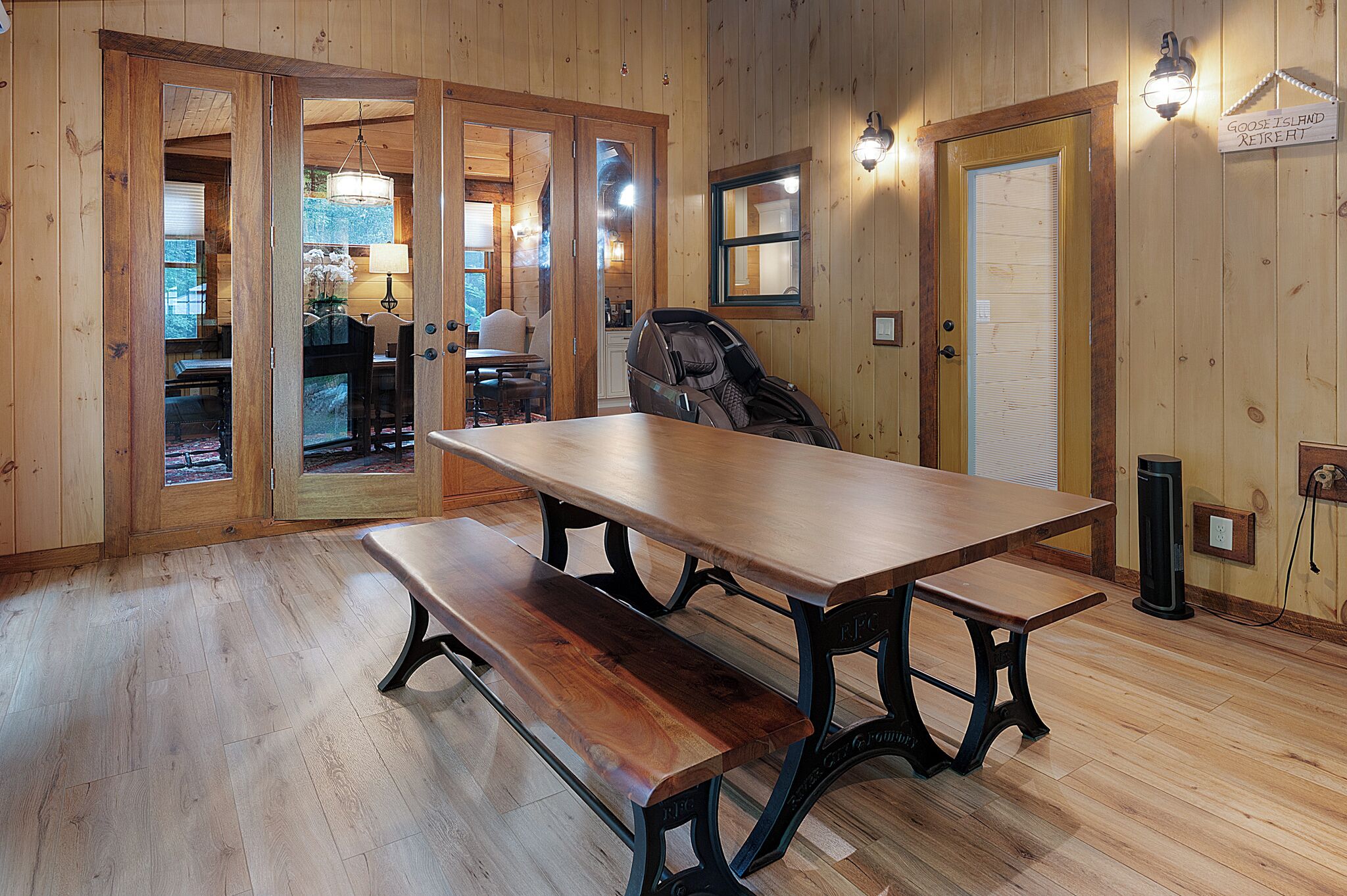A wooden interior with a large table and benches, wooden floors, and a visible door leading to another room.