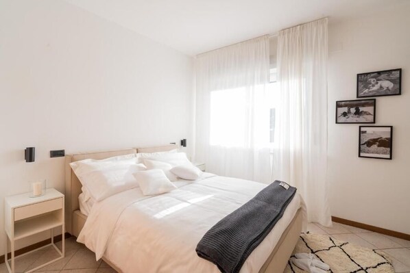 A bedroom with a bed, a bedside table, and a window with curtains.