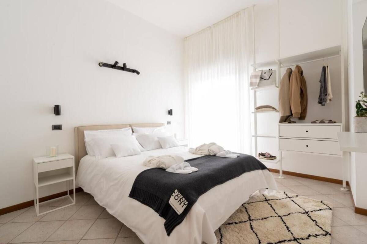 Een moderne hotelkamer met een opgemaakt bed, een nachtkastje, een kledingkast en een groot raam met gordijnen.