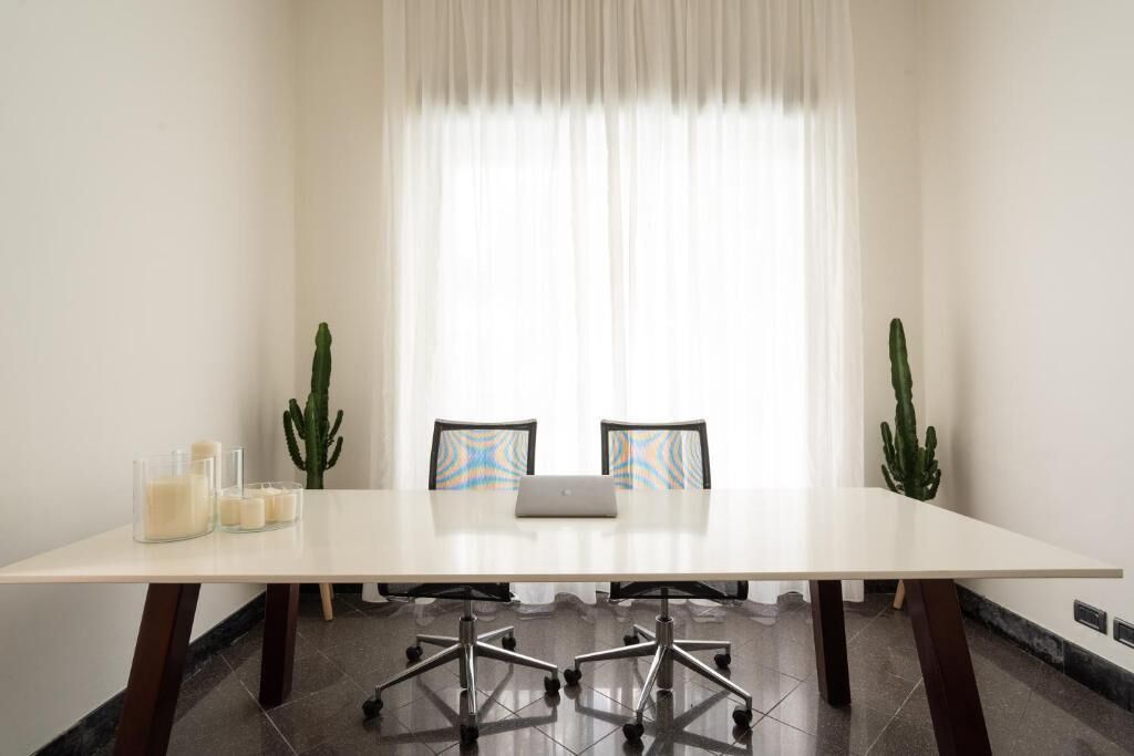 Un salón de conferencias con una mesa blanca, dos sillas, una computadora portátil y tres cactus.