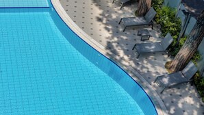 A swimming pool with tiled flooring, surrounded by lounge chairs and a tree. - Hotel Adriatica (Riccione)