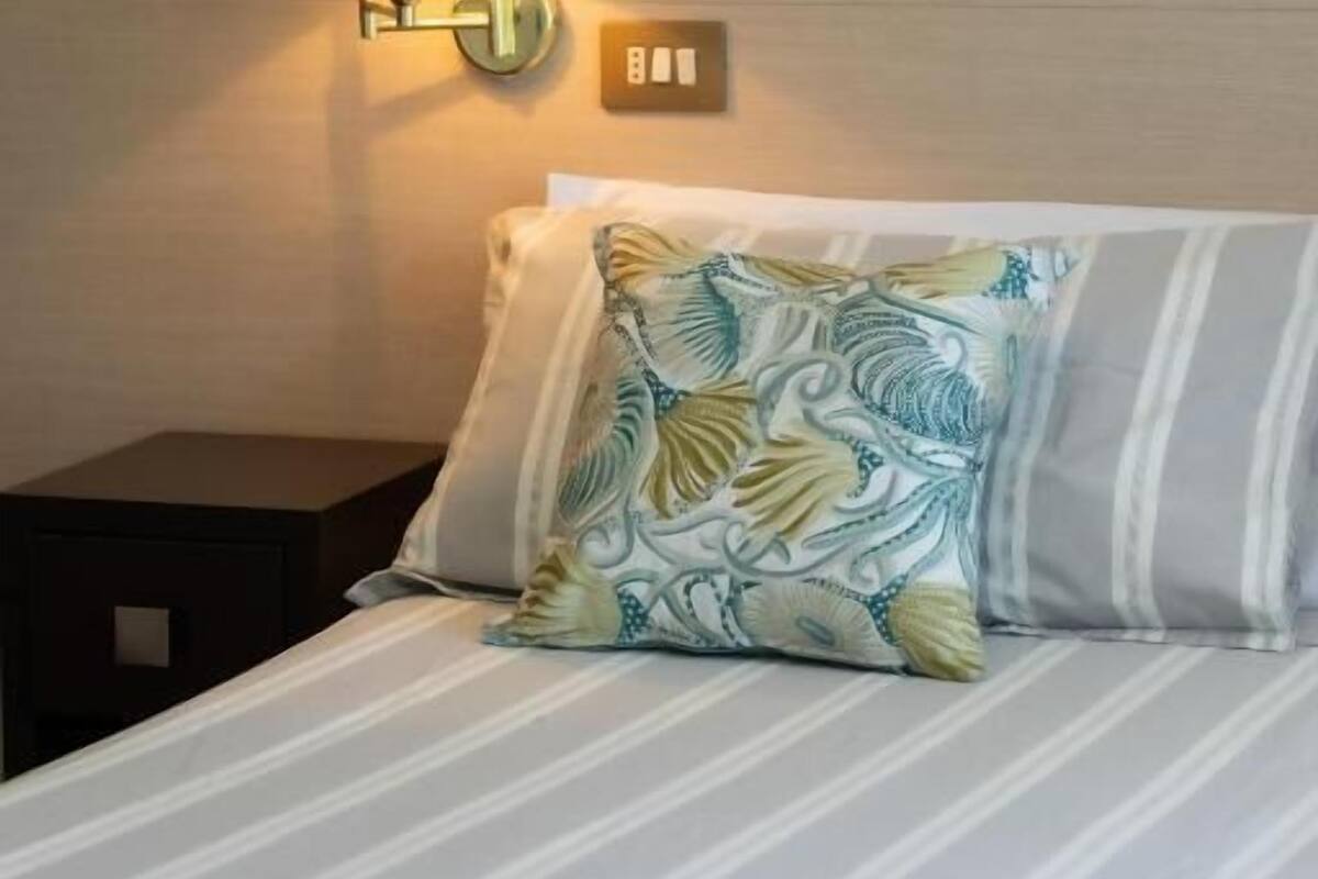 Een hotelkamer met een bed, een nachtkastje, een wandlamp en een lichtschakelaar.