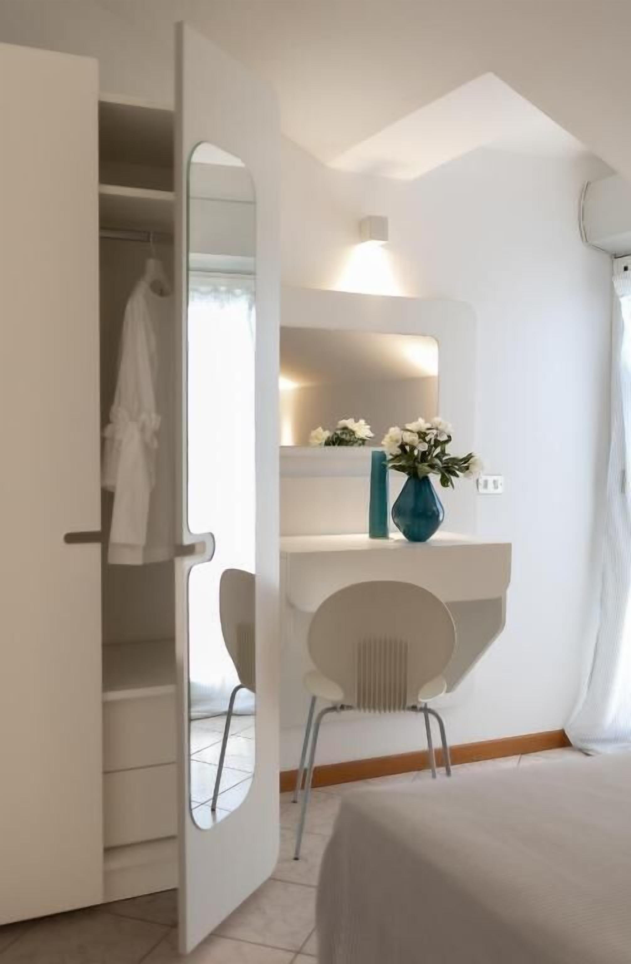 A modern bathroom with a large mirror, a white sink, a vase with flowers, and a shower curtain.