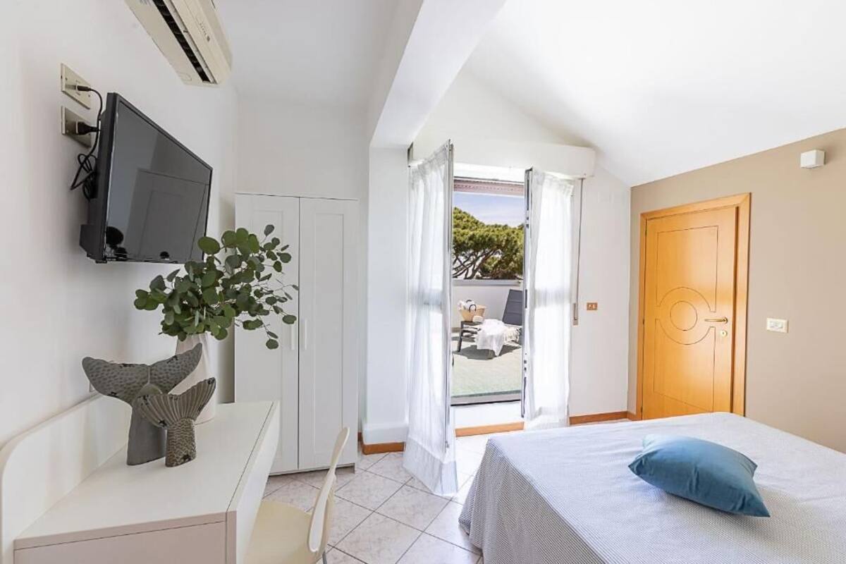 Een slaapkamer met een bed, een aan de muur bevestigde televisie, een plant en een deur naar een buitenruimte.