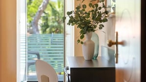 A room with a view of greenery outside, a white chair, and a dark-colored desk with a white vase containing a plant. - Hotel Adriatica (Riccione)