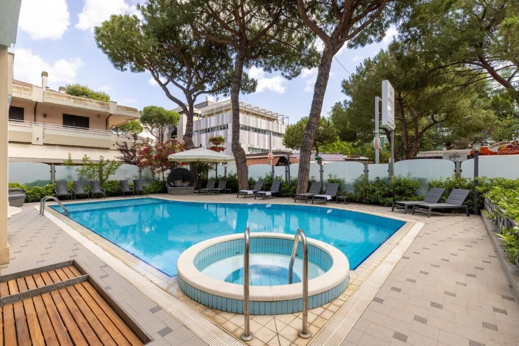 A swimming pool with a hot tub, surrounded by lounge chairs and trees.