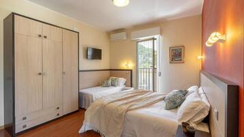 A bedroom with two beds, a wardrobe, a television, and a window with blinds.
