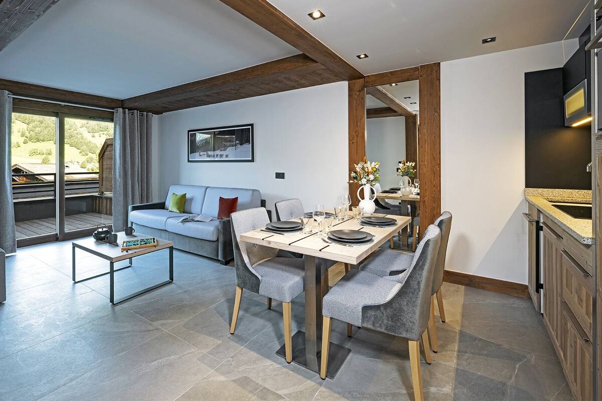 A modern living room with a dining area, wooden ceiling beams, and a kitchen with a built-in oven.
