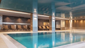 A modern indoor pool with clear blue water, lounge chairs, and a tiled floor.