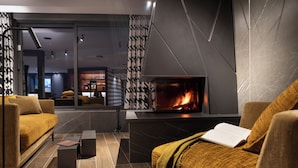 A modern living room with a fireplace, comfortable seating, and a view into the adjacent bar area.