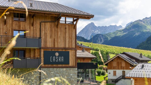 A wooden building with a sign reading 'CASKA' and a view of mountains in the background.