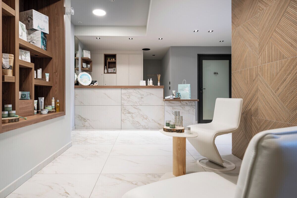 A modern spa area with a reception desk, shelves with products, a seating area, and a wooden wall.
