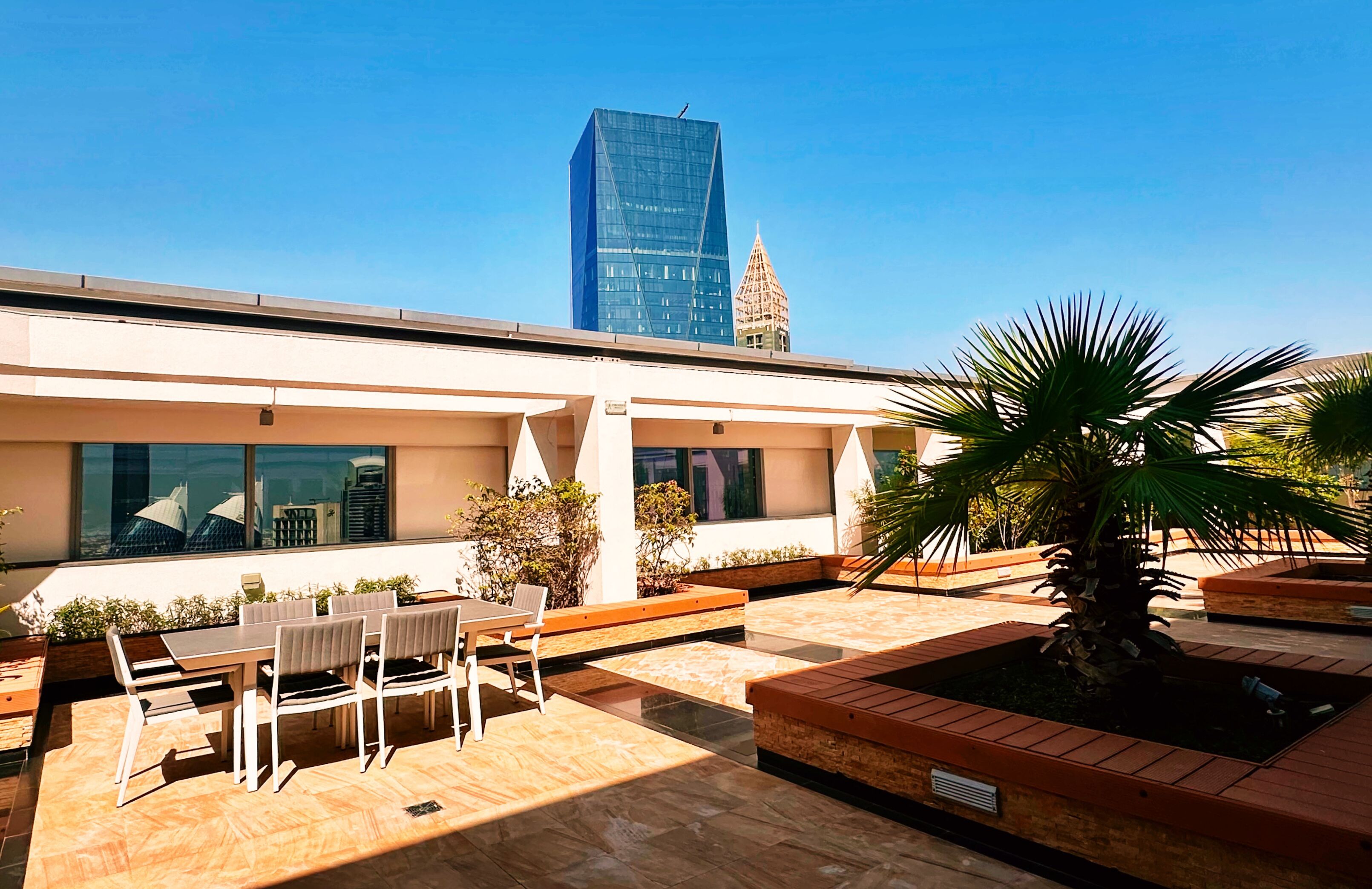 An outdoor patio with a dining area, planters, and a view of a modern building.