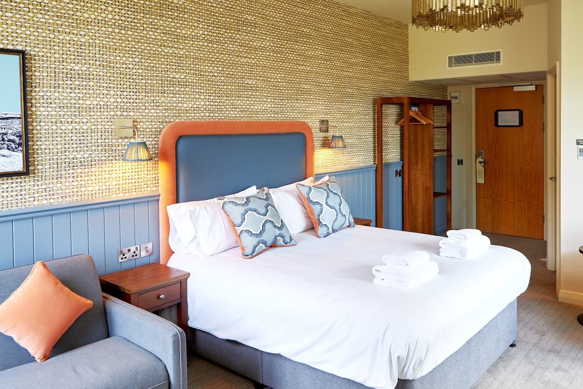 Une chambre d’hôtel bien rangée, avec un grand lit, une table de chevet, une chaise et une petite table.