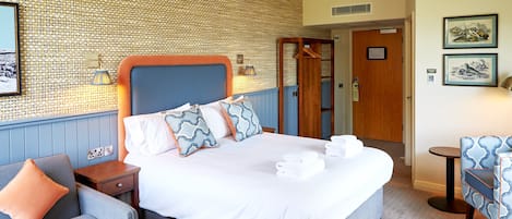 A neatly arranged hotel room with a large bed, a bedside table, a chair, and a small table.
