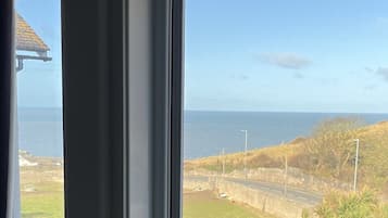 Vista desde una ventana con vista a una carretera costera, cielo despejado y el mar al fondo.