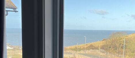 A view from a window overlooking a coastal road with a clear sky and the sea in the distance.