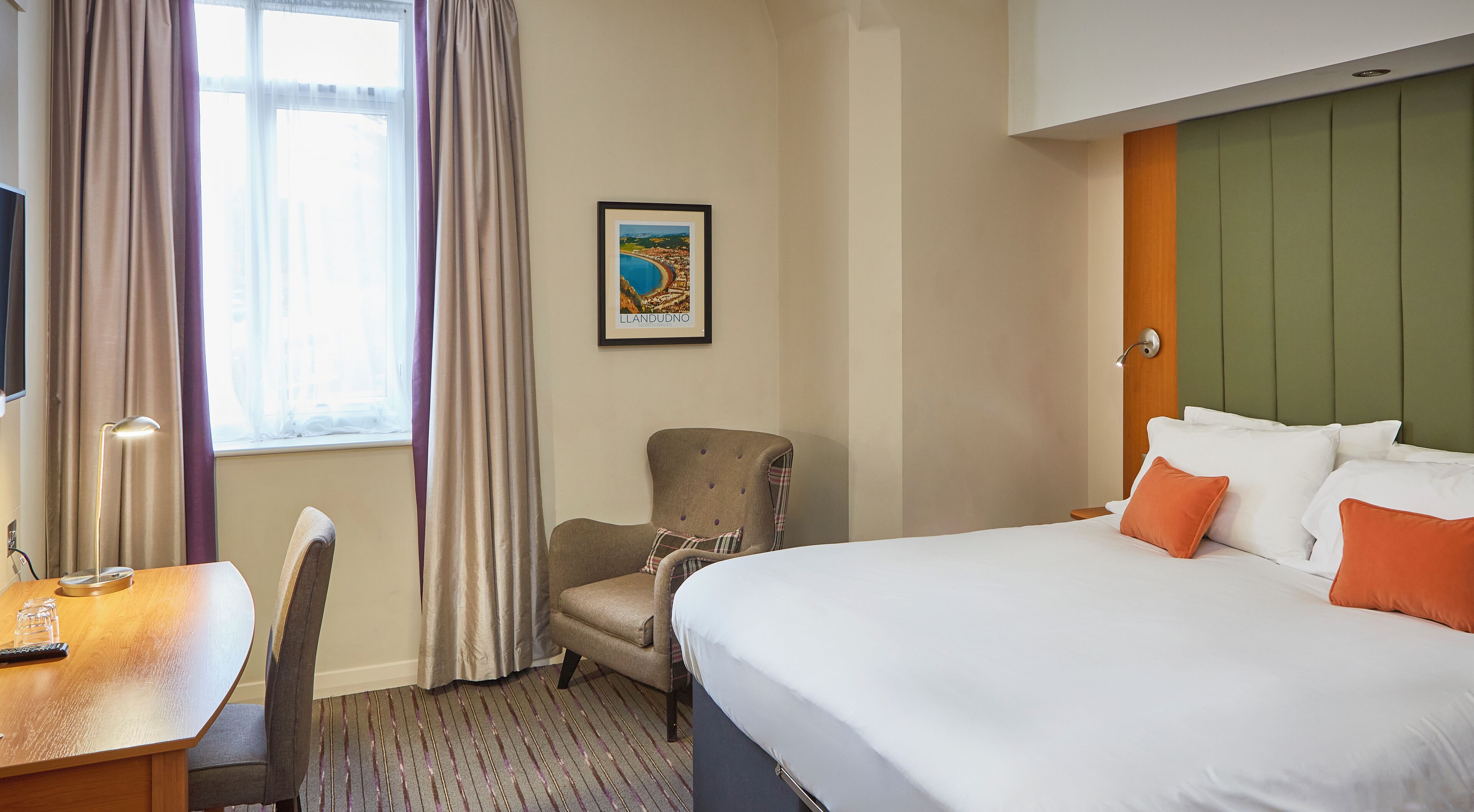 A hotel room with a bed, a desk, a chair, and a window with curtains.